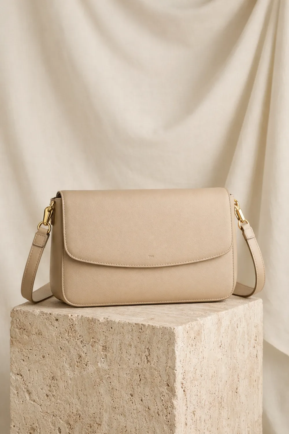 Minimal beige leather crossbody handbag on stone pedestal