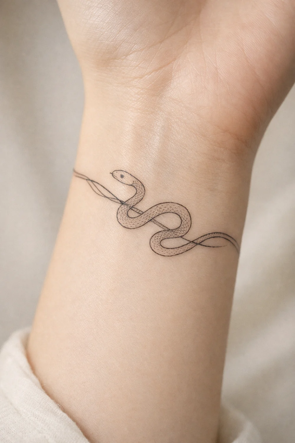 minimalist snake wrist tattoo with delicate linework wrapping around the wrist, elegant fine line snake tattoo design symbolizing transformation protection and personal power