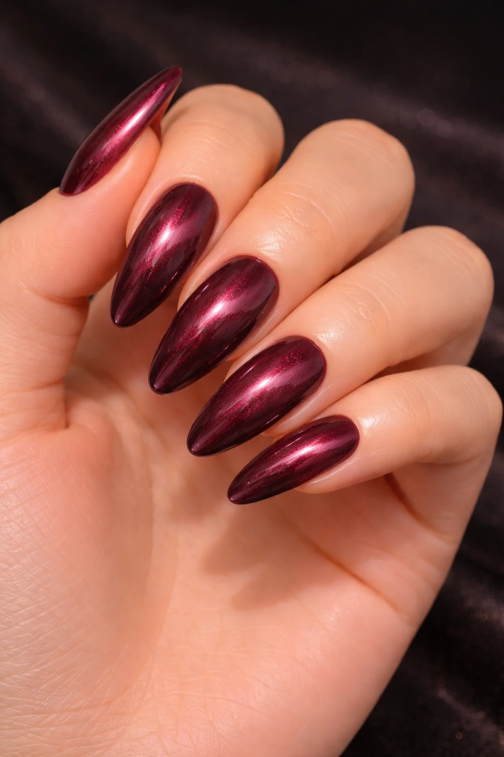Deep burgundy chrome acrylic nails with glossy metallic finish on long almond shaped nails creating a bold glamorous manicure perfect for luxury nail inspiration.