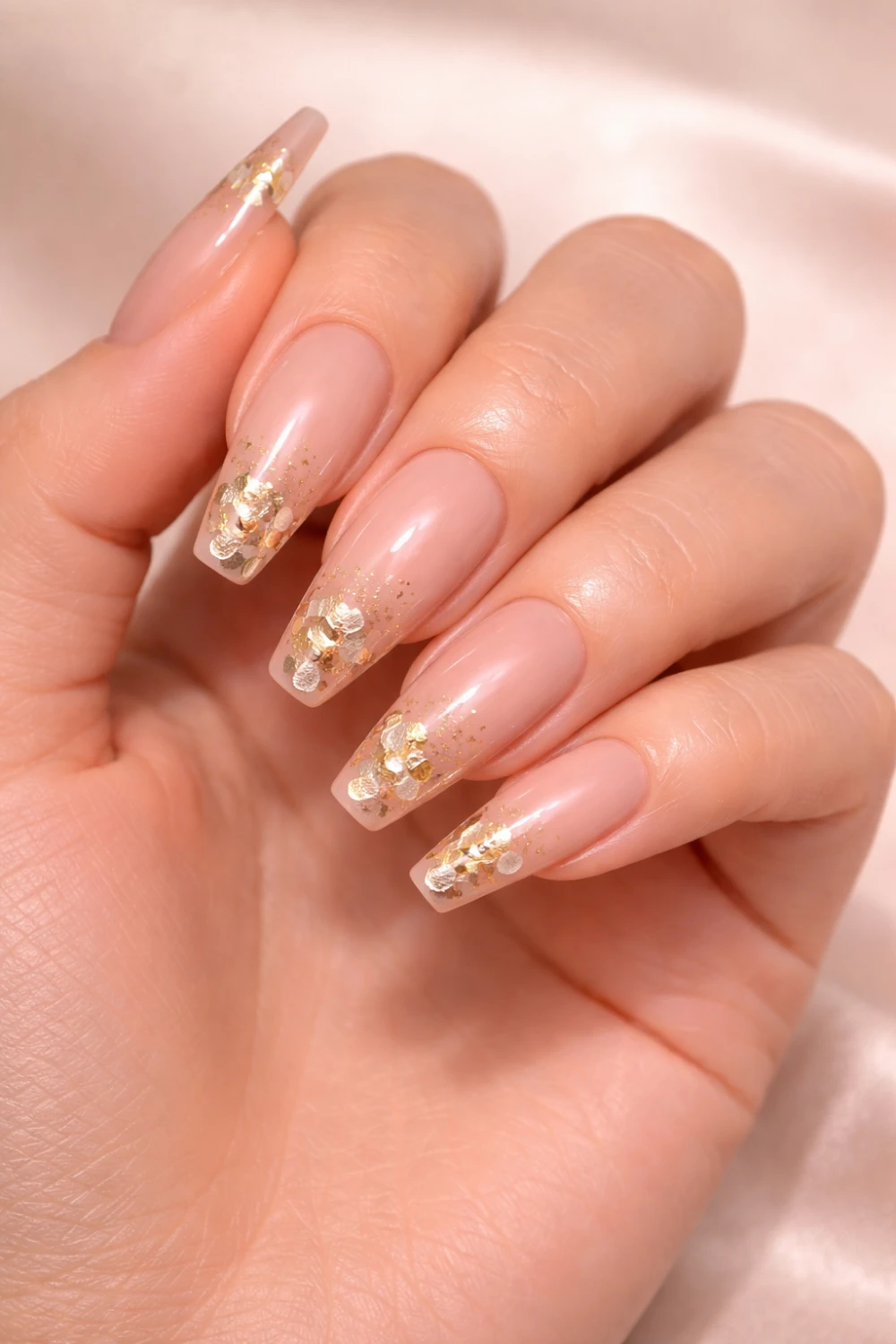 Nude acrylic nails with delicate gold foil accents on long coffin shaped nails creating a soft glamorous manicure perfect for elegant nail inspiration.