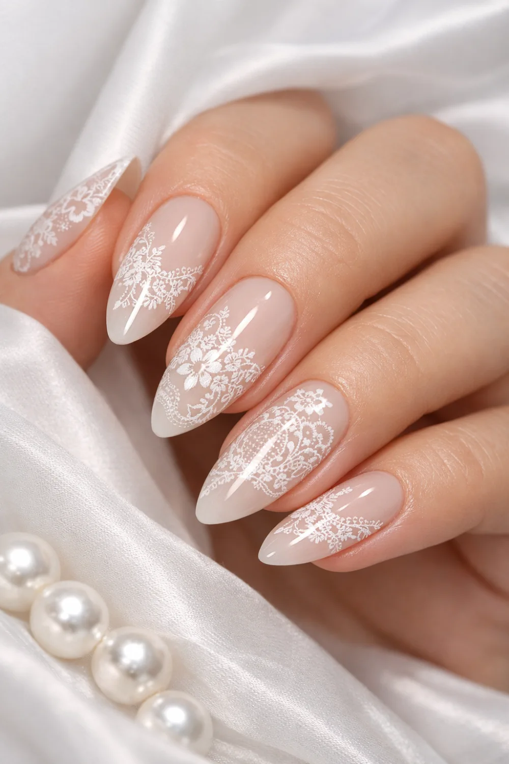 Elegant almond shaped bridal manicure featuring delicate white lace nail art over a soft milky nude base with glossy gel finish, intricate floral lace patterns inspired by wedding lace fabric creating a romantic and classy bridal nail look perfect for elegant manicure inspiration and trending wedding nail designs