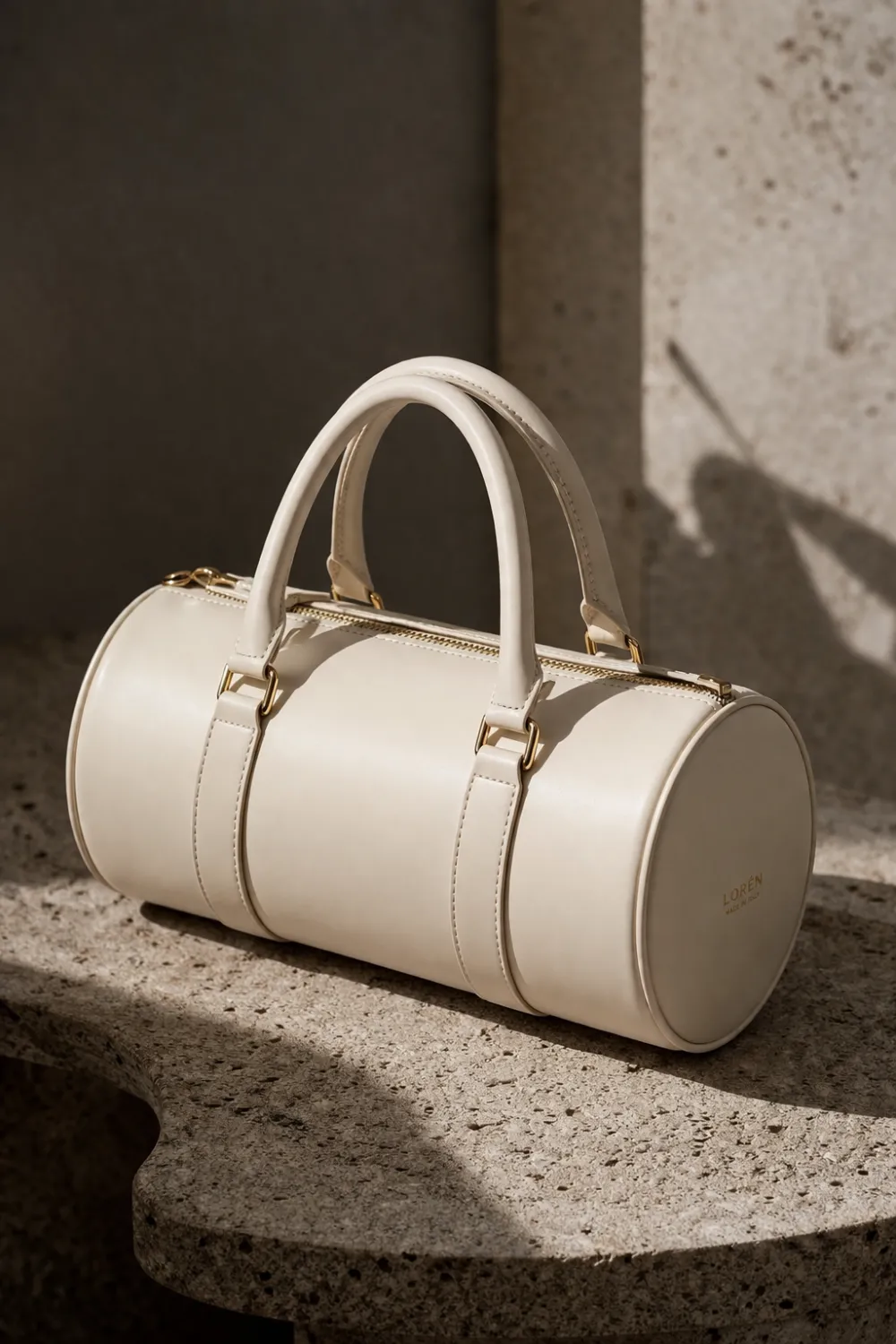 Cream leather cylindrical barrel handbag with structured shape placed on stone surface, modern barrel bag trend for women fashion 2026.