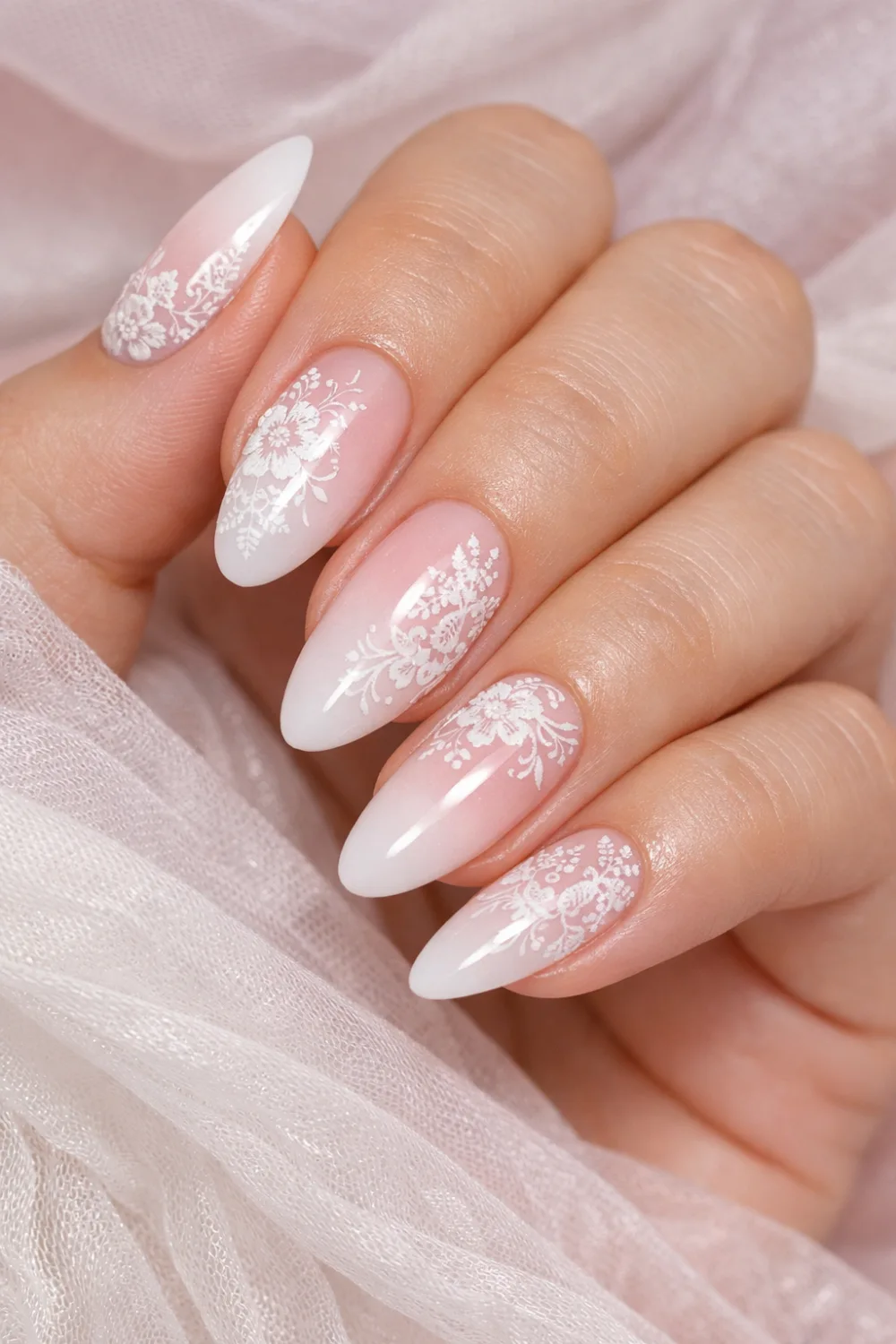 Soft pink to white ombre manicure with delicate lace floral patterns over almond shaped nails, romantic gradient lace nail design creating an elegant feminine manicure perfect for bridal nail inspiration