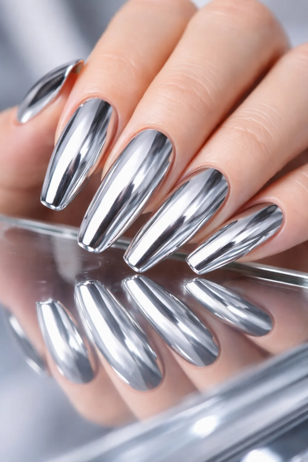 Silver chrome mirror nails with liquid metal reflection on long almond nails, ultra glossy metallic manicure reflecting light beautifully, modern futuristic chrome nail design inspiration for trendy manicures