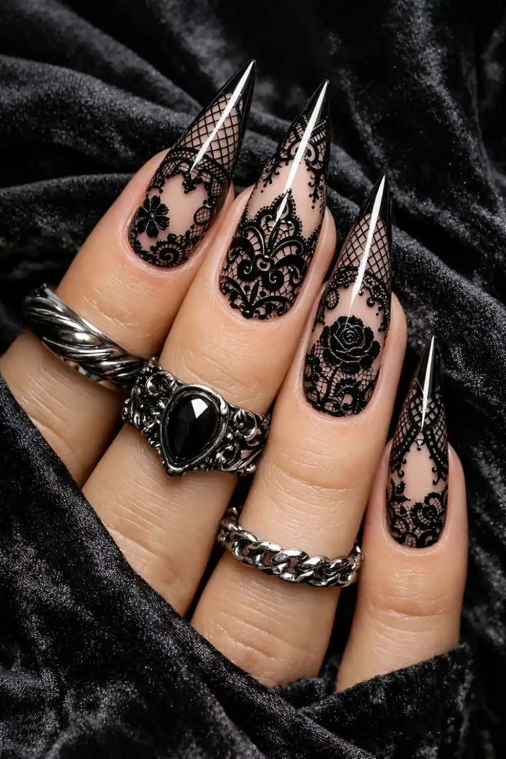 Bold black gothic lace nail design with long stiletto nails featuring intricate black lace patterns over a nude base polish, dramatic glossy manicure with mesh lace details perfect for edgy gothic nail inspiration and elegant dark manicure trends