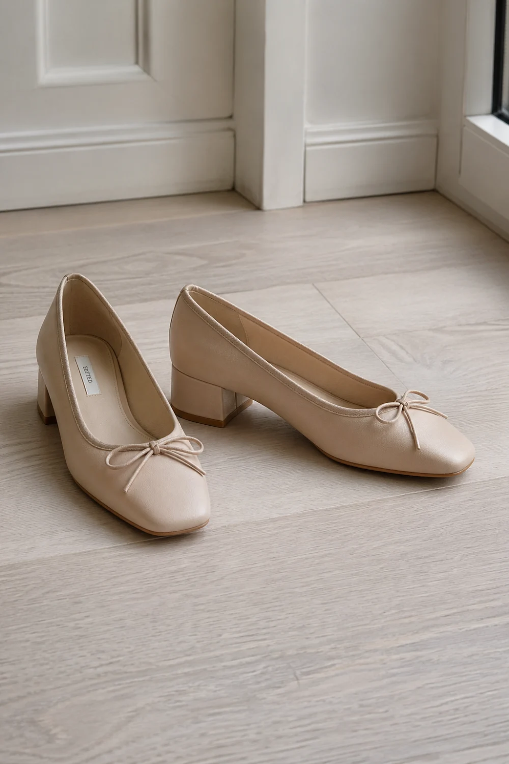 Beige ballet heels with low block heel and soft leather finish placed on light wooden floor, elegant feminine footwear with bow detail, minimal luxury style, perfect for chic everyday outfits and refined spring looks