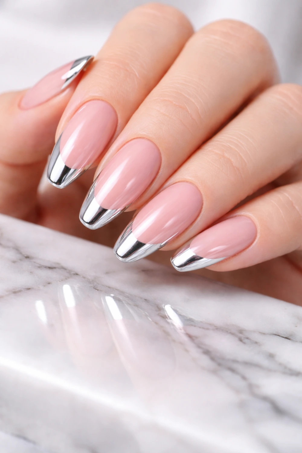 Elegant chrome French tip nails with soft nude pink base and shiny metallic silver tips, modern minimalist manicure design photographed on marble surface, stylish chrome French nail inspiration