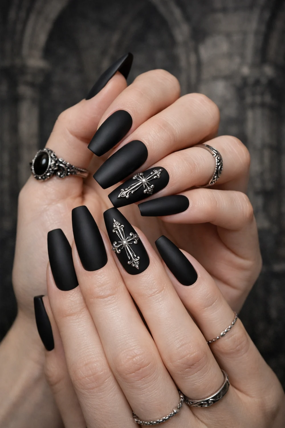 Matte black coffin nails with silver gothic cross accents, elegant dark glam manicure on long coffin shaped nails paired with gothic rings and dramatic gothic aesthetic style.