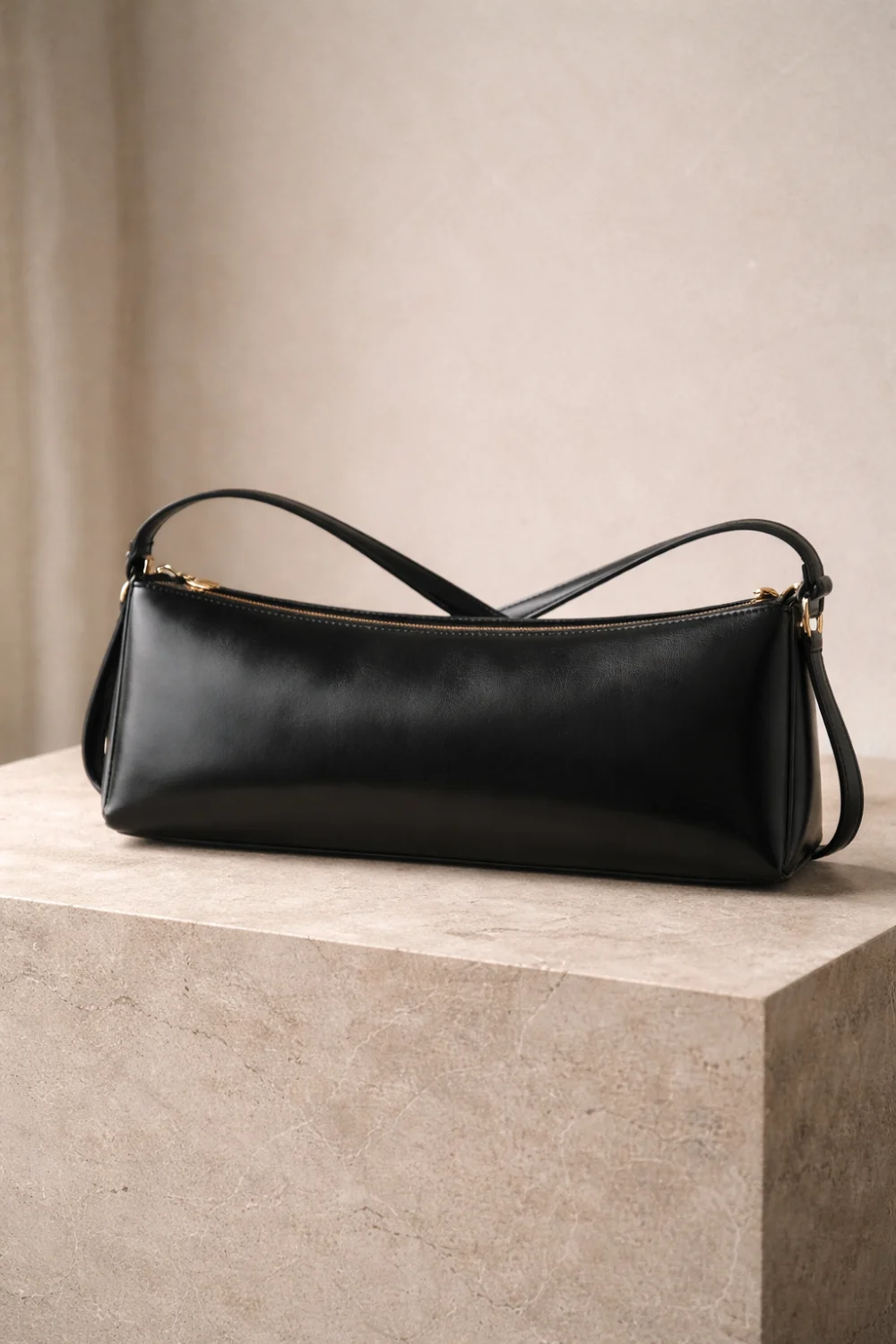 Sleek black east west shoulder handbag with long horizontal shape placed on stone display, modern minimalist handbag trend for women fashion 2026.