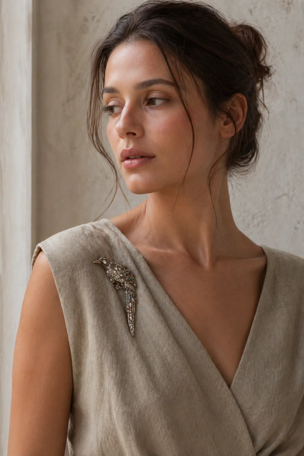 Female model in a neutral linen dress styled with a vintage bird-inspired crystal brooch on the shoulder, natural daylight, minimal makeup, earthy tones, refined and organic fashion look