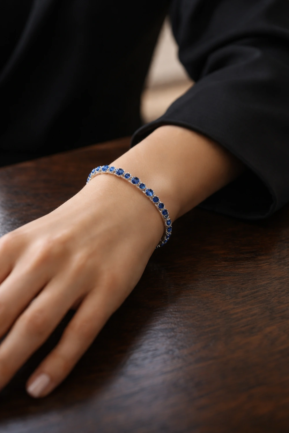 Close up of a sapphire tennis bracelet worn on a wrist with a dark outfit, highlighting deep blue gemstones that create a sophisticated and timeless old money jewelry look.