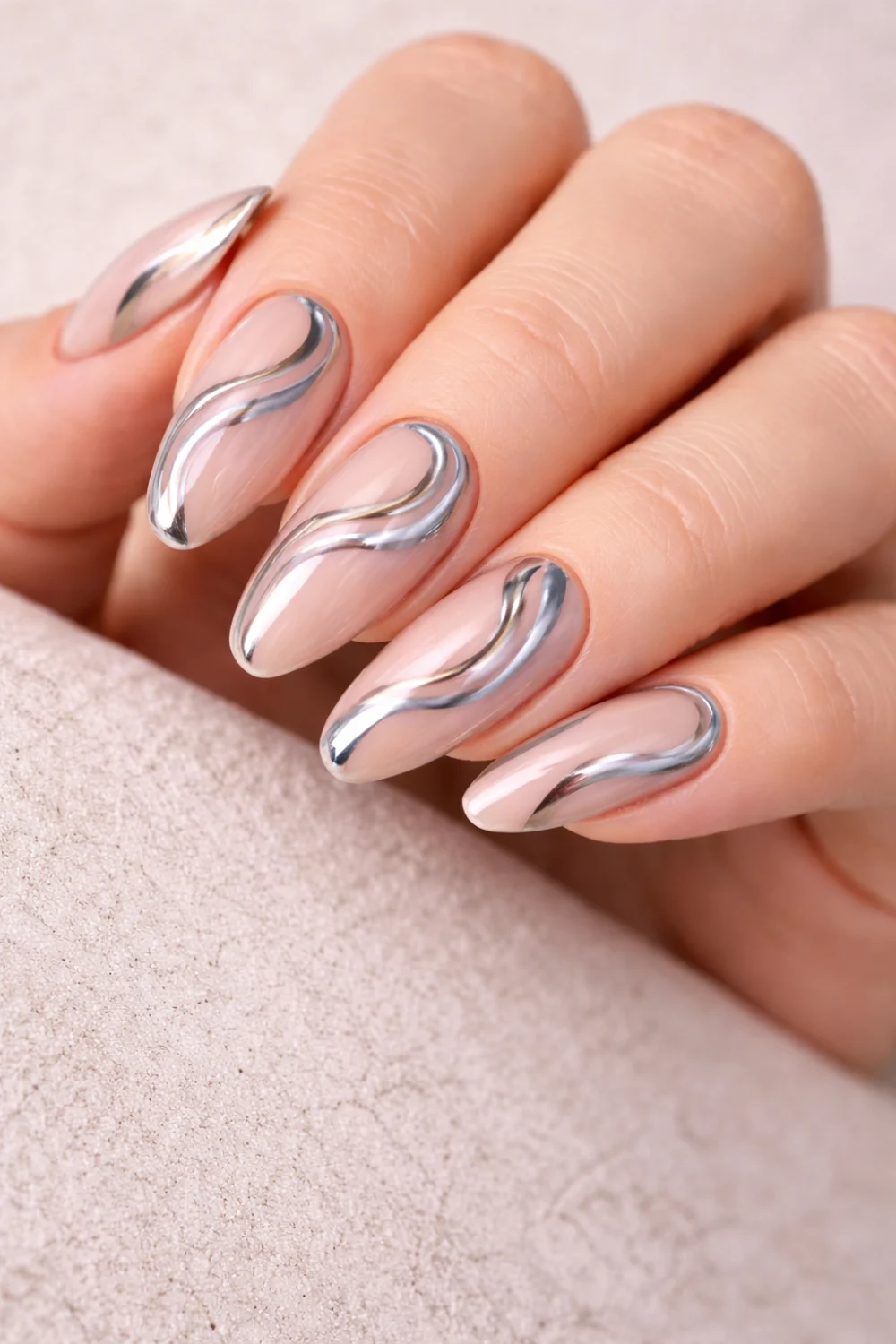 Nude nails with silver chrome swirl nail art on almond shaped manicure, glossy neutral base with reflective metallic swirl lines, modern chrome swirl nail design inspiration
