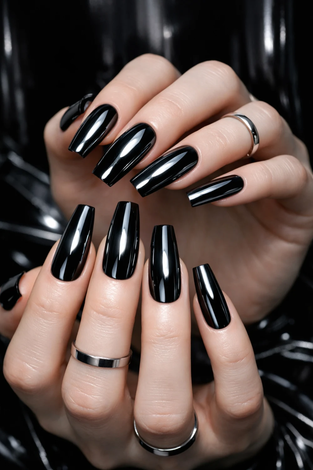 Glossy black coffin nails on elegant hands with silver rings, sleek dark glam manicure featuring long coffin shaped nails perfect for gothic aesthetic nail inspiration.