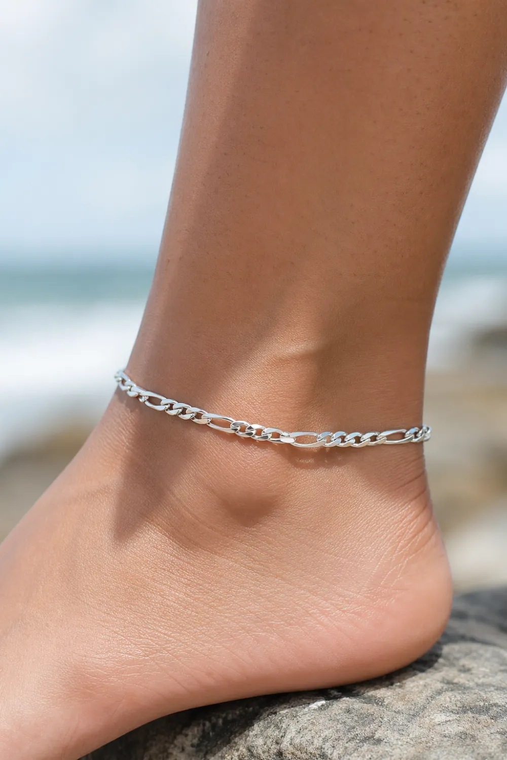 silver chain anklet on ankle beach rock close up cool toned minimal ankle bracelet modern summer jewelry style