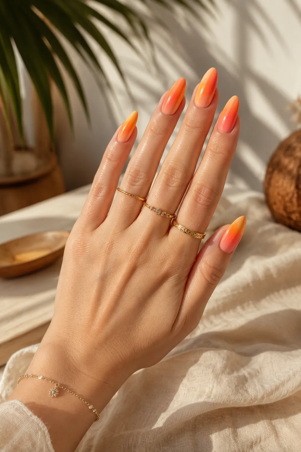 Glossy sunset orange ombre nails with peach, coral, and warm tropical gradient on long almond-shaped nails, styled with gold rings and soft summer lighting for trendy 2026 manicure inspiration.