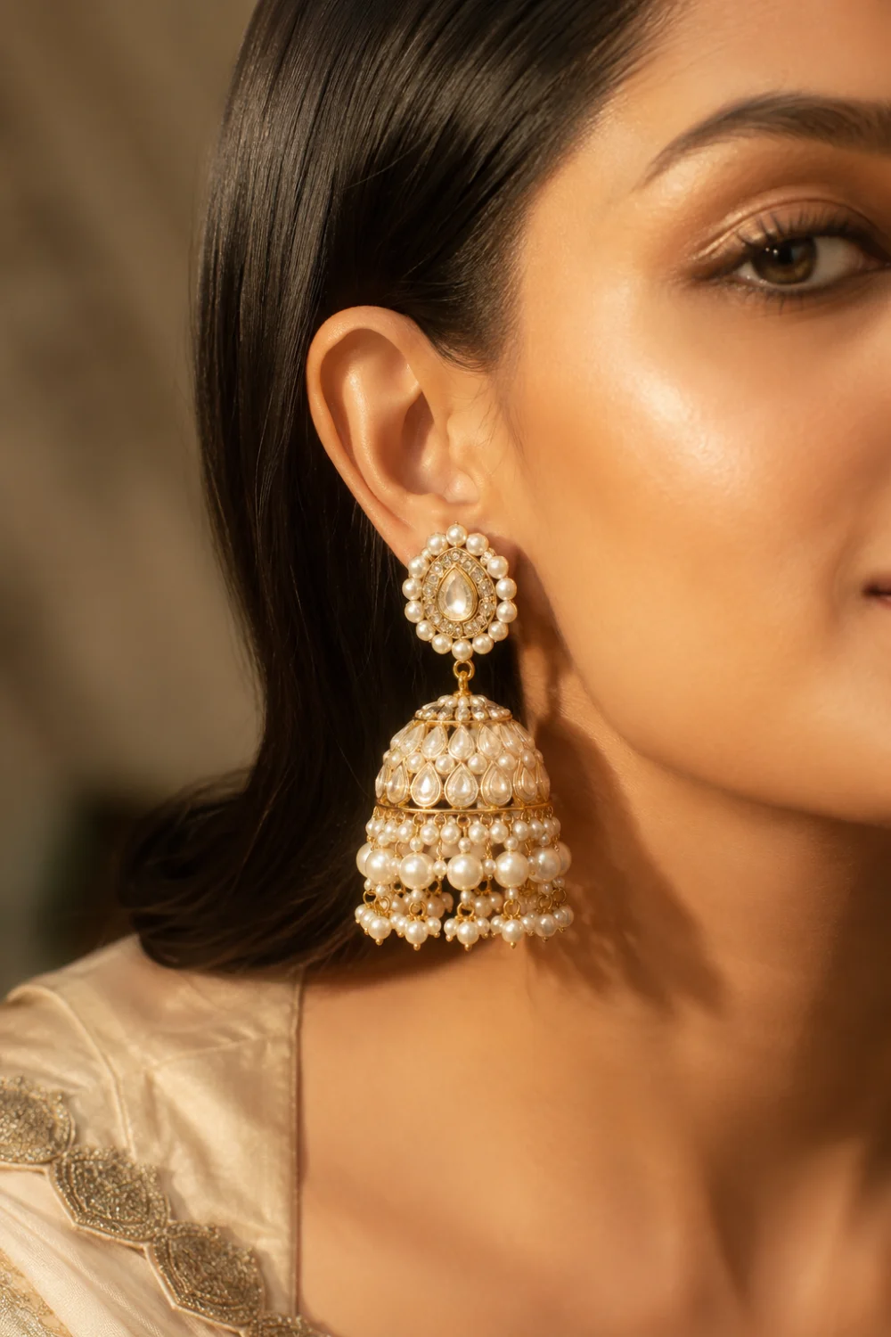 Close-up portrait of a woman wearing modern pearl dome gold jhumka earrings featuring layered pearl tassels, glossy gold detailing, luxury bridal craftsmanship, and elegant ethnic fashion styling with soft glam makeup and warm lighting