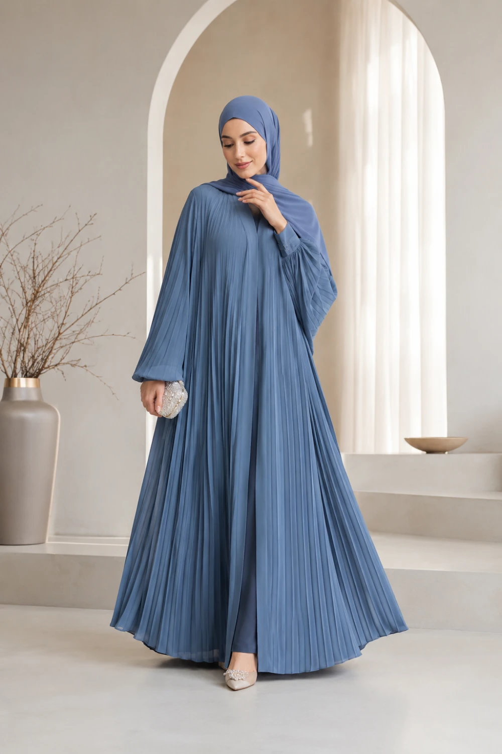 Muslim woman wearing dusty blue pleated abaya with matching hijab and flowing modest silhouette full body luxury indoor fashion shoot