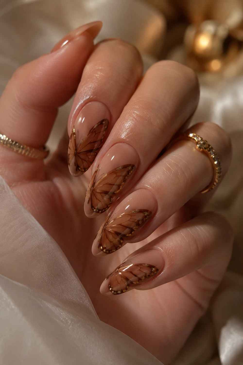 Nude brown glossy almond nails with elegant butterfly wing nail art, warm-toned feminine manicure design, shiny gel polish, and classy salon-style nails.