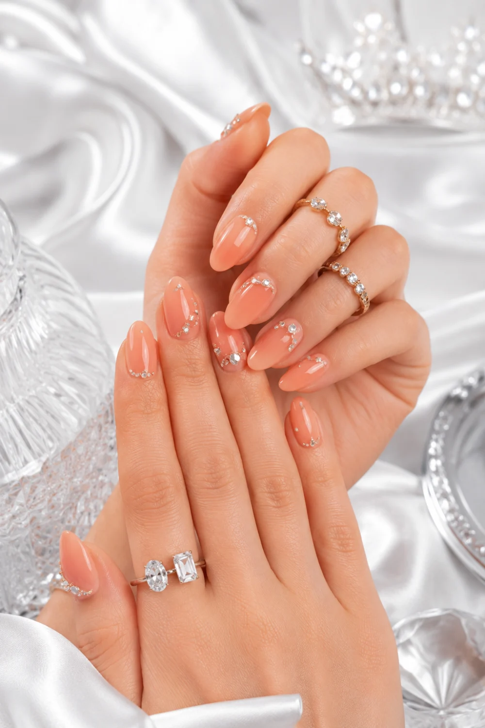 Peach rhinestone glam nails with glossy almond manicure, crystal nail accents, luxury rings, and elegant feminine styling