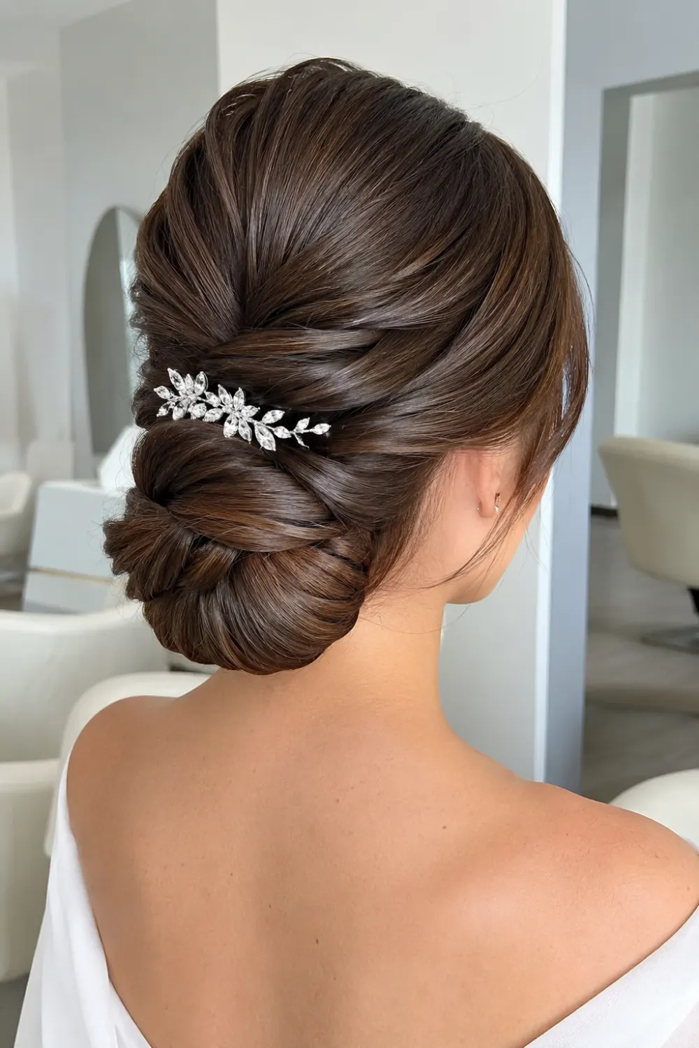 Sleek twisted bridal bun hairstyle with smooth twisted sections, polished low bun, glossy brunette hair, and elegant crystal hair accessory for weddings.