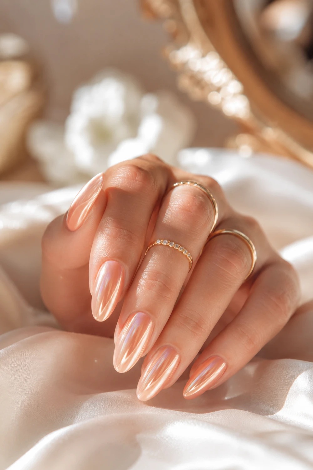 Glossy peach chrome glazed nails with reflective pearly shine, luxury gold rings, and elegant feminine clean girl nail aesthetic