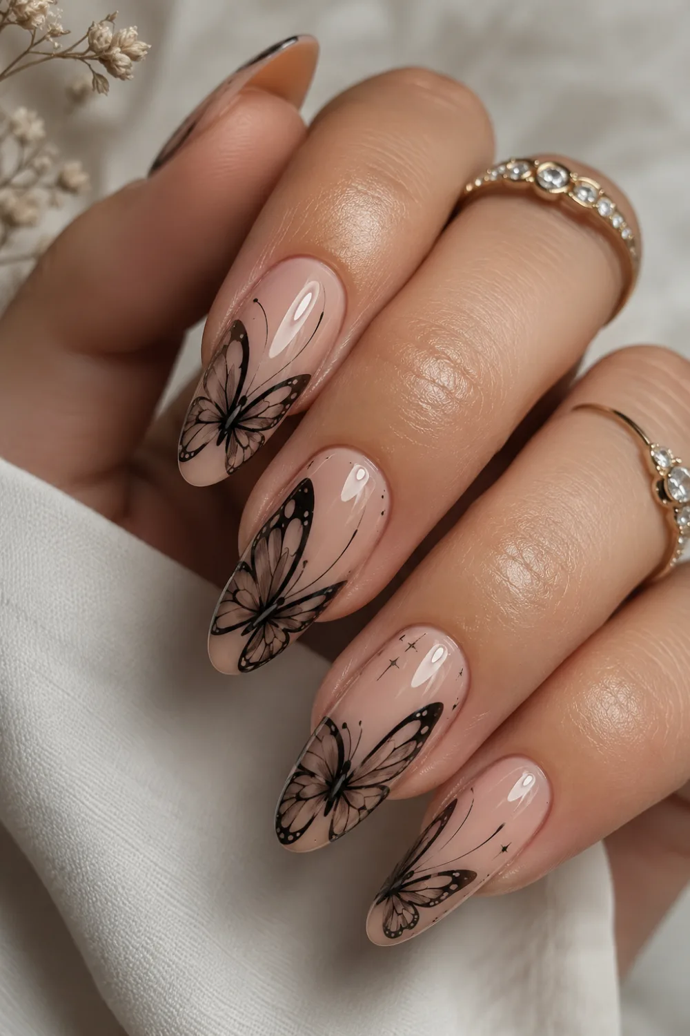 Glossy nude almond nails with black butterfly wing nail art, elegant minimalist manicure design, shiny gel polish, and classy feminine butterfly nails with luxury salon finish.