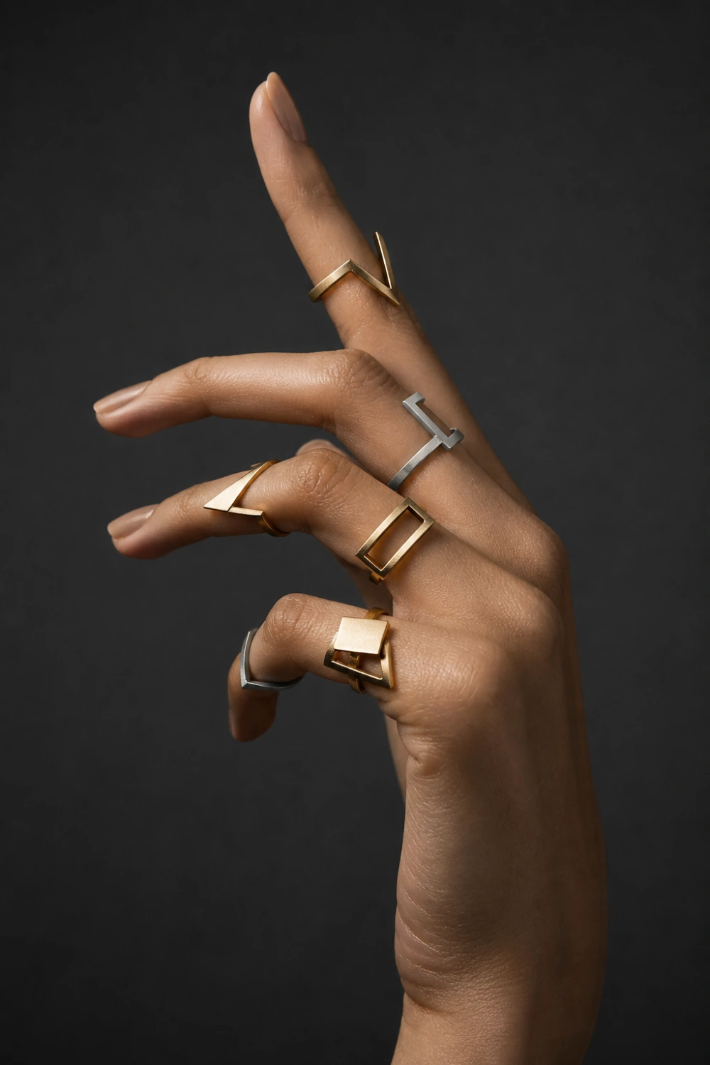 female hand wearing geometric knuckle rings with sharp shapes in gold and silver, modern abstract midi rings, dark background, editorial fashion jewelry style, bold minimalist design, high contrast lighting