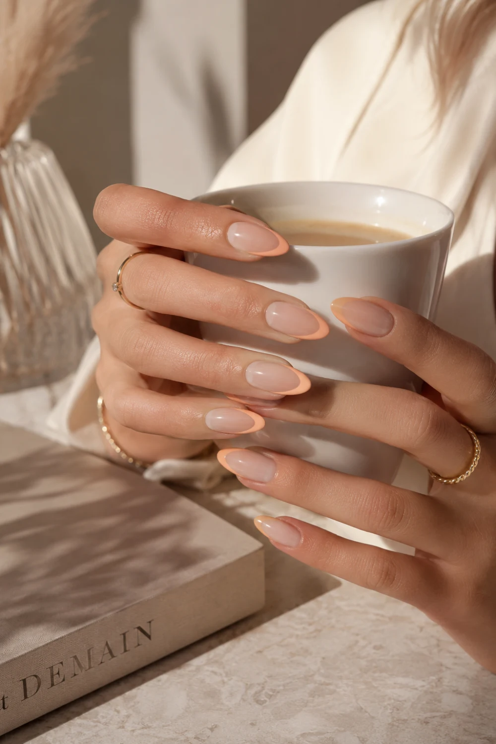 Peach French tip almond nails with nude glossy base, elegant feminine hands, gold jewelry, and classy summer manicure styling