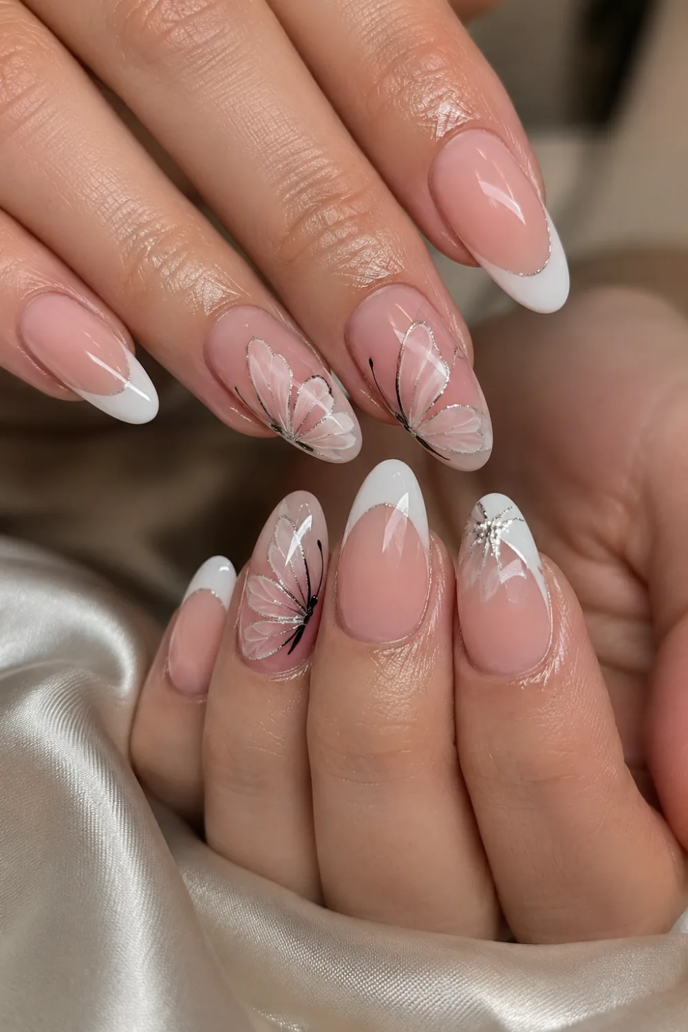 Glossy French tip almond nails with elegant butterfly wing nail art, nude pink gel polish, white French tips, and classy feminine salon manicure design.