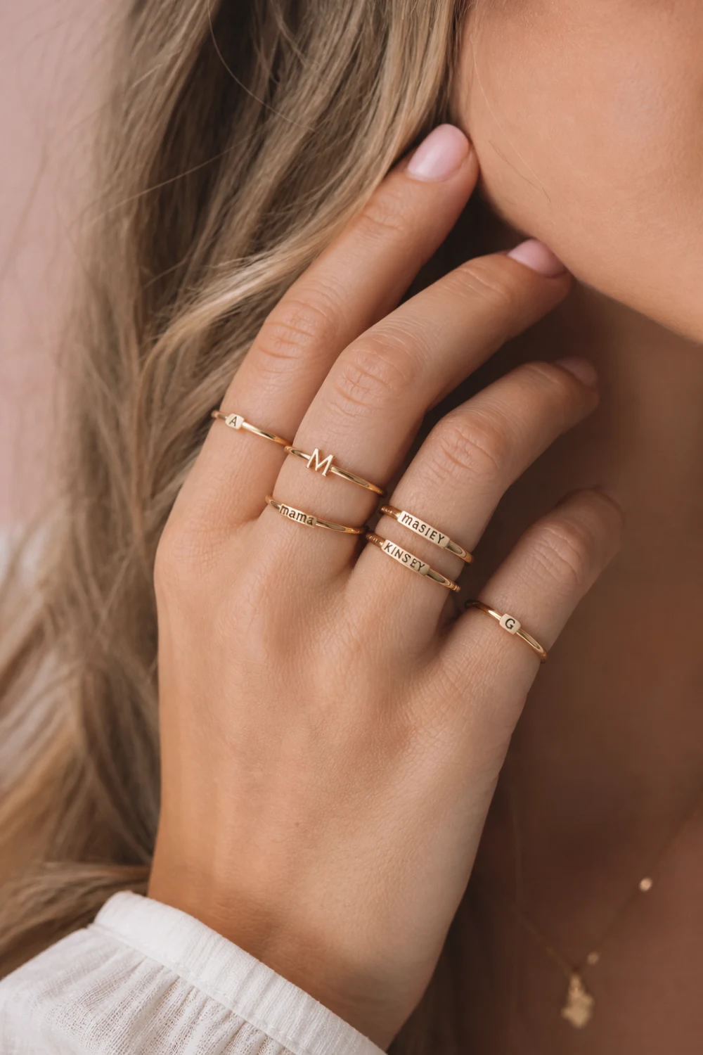female hand wearing personalized name and initial knuckle rings in gold, engraved midi rings, soft pastel background, clean manicure, minimal jewelry aesthetic, custom rings close-up