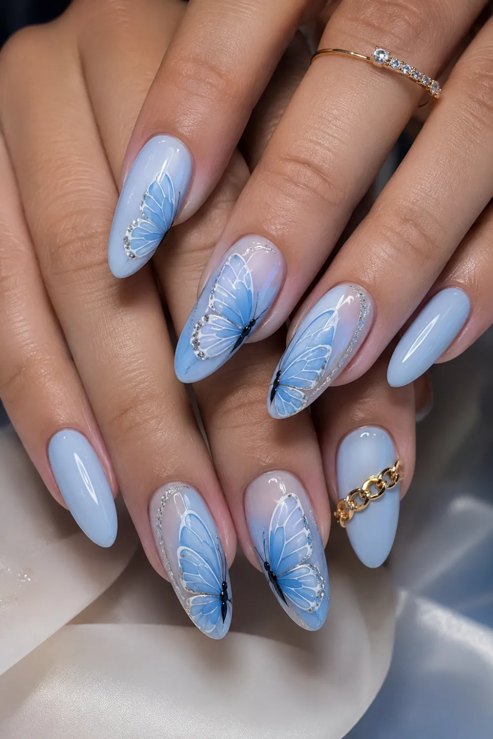 Pastel blue glossy almond nails with butterfly wing nail art, elegant feminine manicure design, silver glitter accents, and classy salon-style butterfly nails.