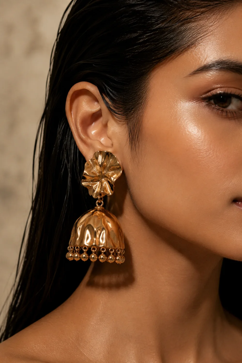 Modern sculpted designer gold jhumka earrings with glossy artistic metalwork, contemporary runway-inspired styling, and luxury fashion editorial aesthetic on female model