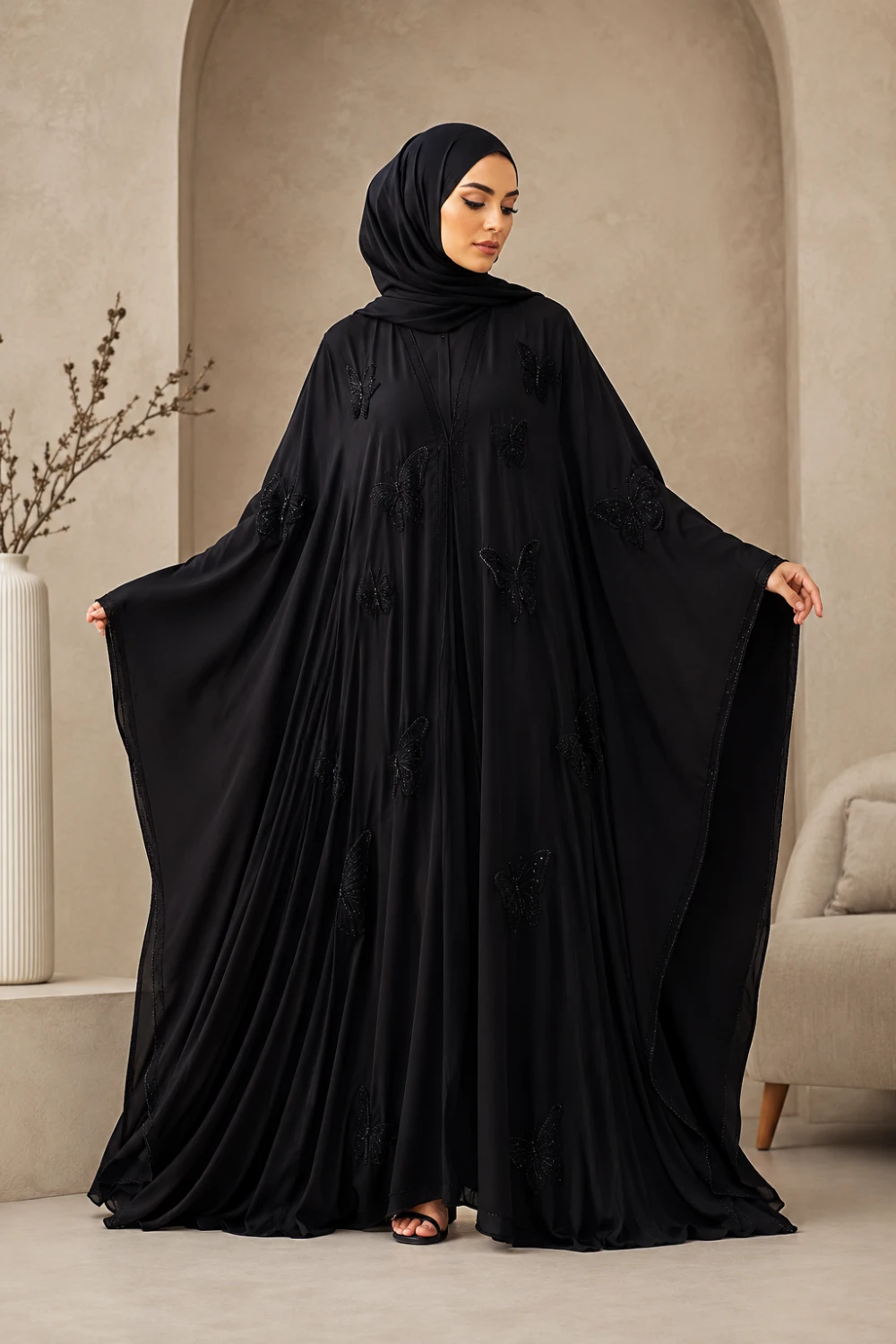 Muslim woman wearing black butterfly embellished abaya with flowing oversized sleeves and matching hijab full body modest fashion portrait