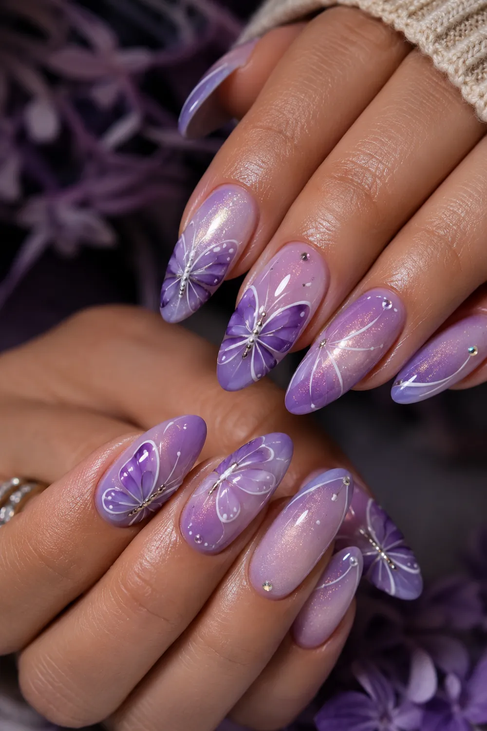Purple butterfly glitter almond nails with glossy ombré nail design, elegant butterfly wing art, rhinestone accents, and feminine salon-style manicure.
