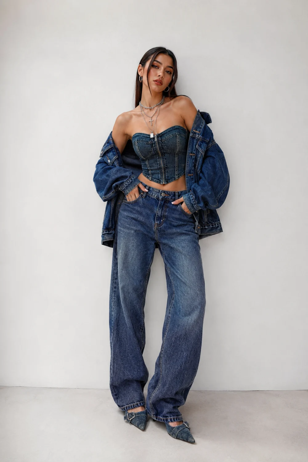 Stylish woman wearing denim corset top with baggy jeans and oversized denim jacket, trendy Y2K night out outfit idea, cool denim-on-denim women’s fashion aesthetic with layered silver jewelry and pointed heels.