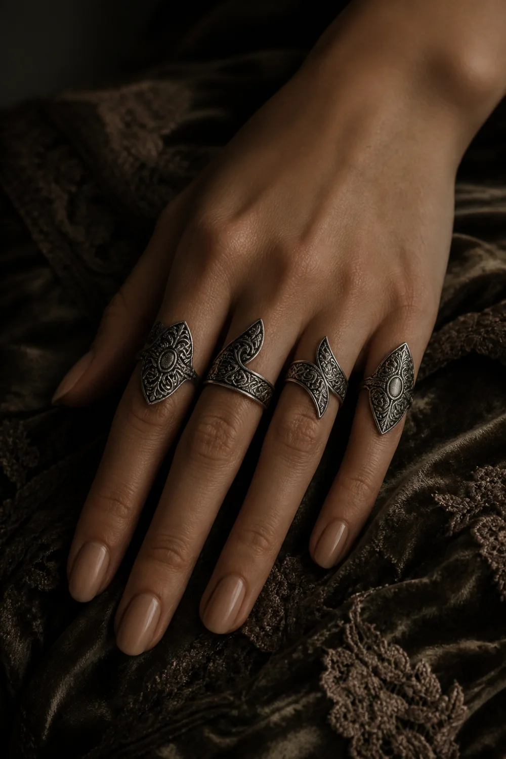 female hand wearing vintage inspired knuckle rings with engraved silver patterns, antique style midi rings, dark moody background, textured fabric, classic jewelry aesthetic, old money style
