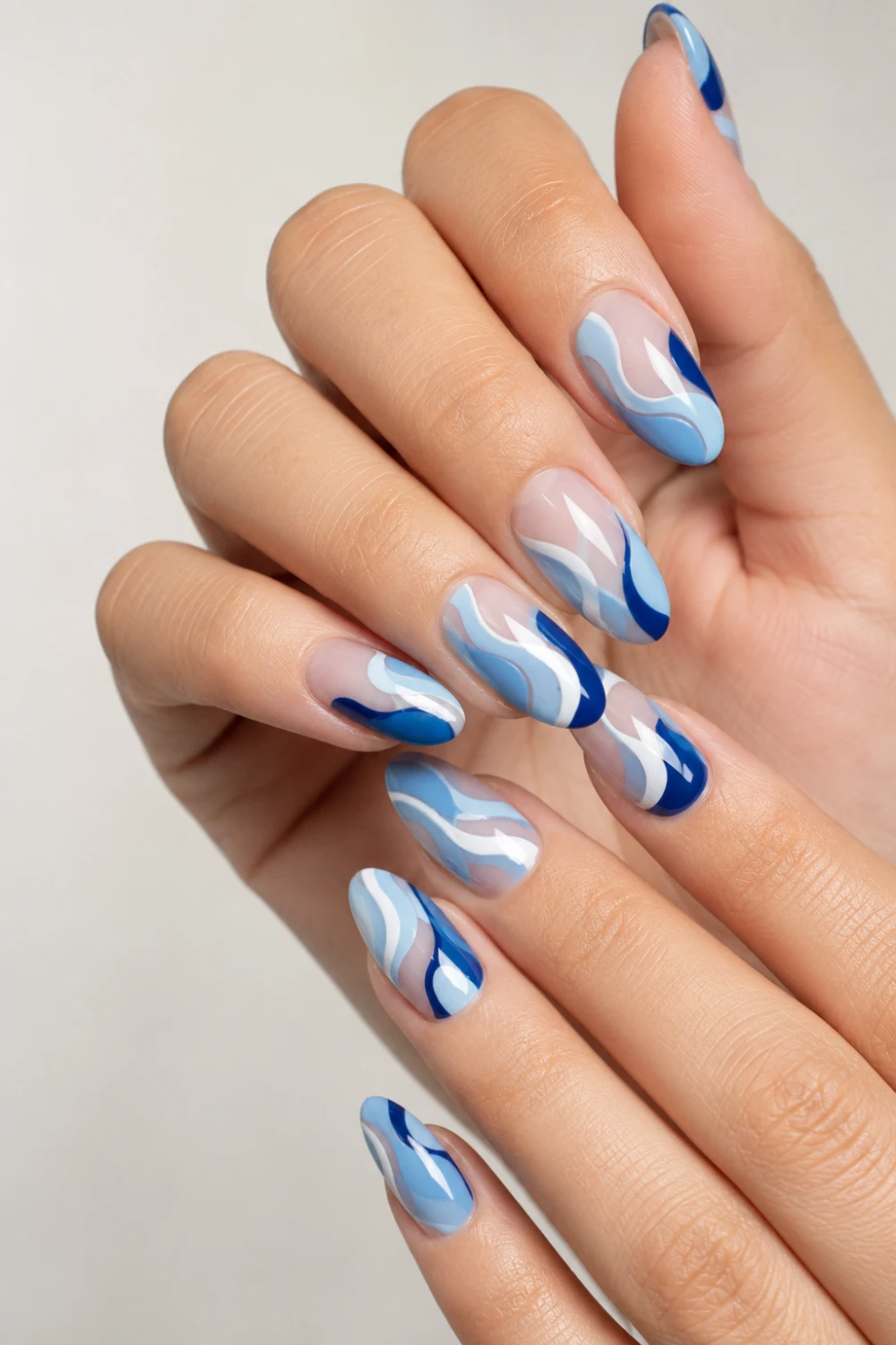 Blue swirl abstract almond nails with flowing wave nail art, glossy pastel and royal blue manicure featuring trendy Pinterest-inspired modern nail design.