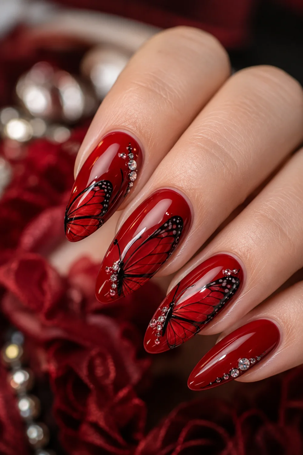 Glossy red almond nails with black butterfly wing nail art, rhinestone accents, luxury feminine manicure design, and bold glamorous butterfly nails.