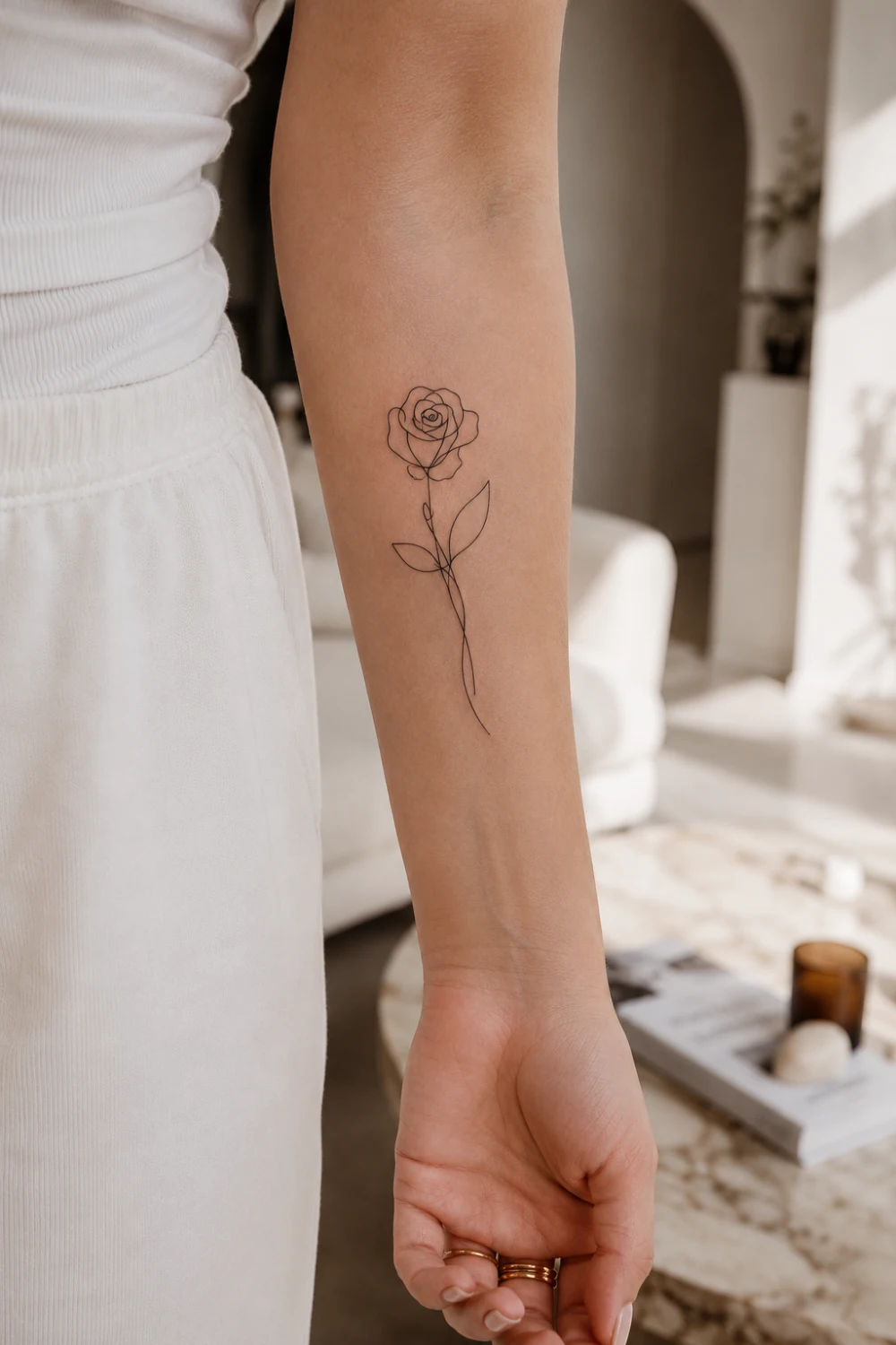 Elegant single line rose tattoo on a woman's inner forearm featuring delicate fine line floral artwork, minimalist black ink rose design, feminine tattoo inspiration, modern aesthetic tattoo style, and timeless botanical body art.