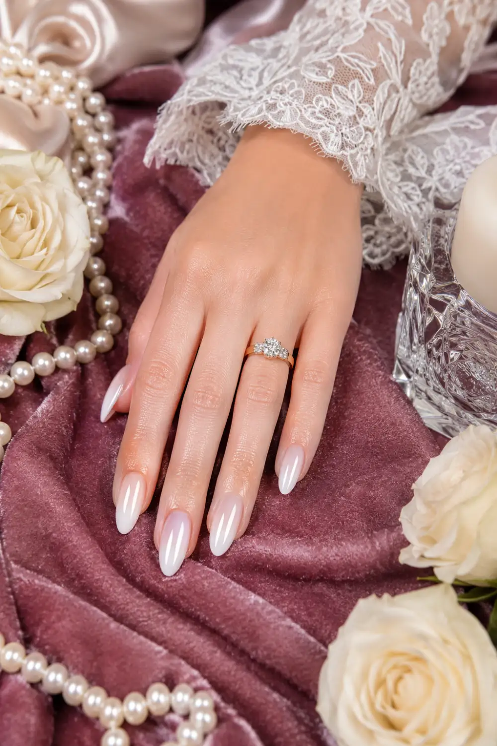 Classic pearl glazed donut nails with luminous chrome finish on almond shaped nails, elegant bridal manicure on mauve velvet fabric with pearls, white roses, luxury nail trend inspiration for Pinterest