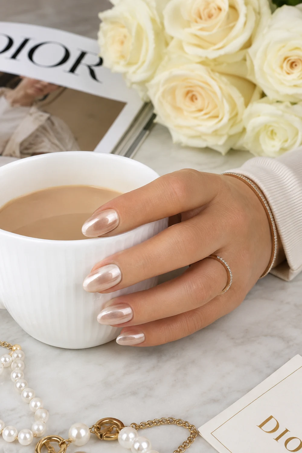 Champagne glazed donut nails with glossy metallic chrome finish, elegant neutral manicure holding coffee cup with luxury jewelry and feminine styling inspiration