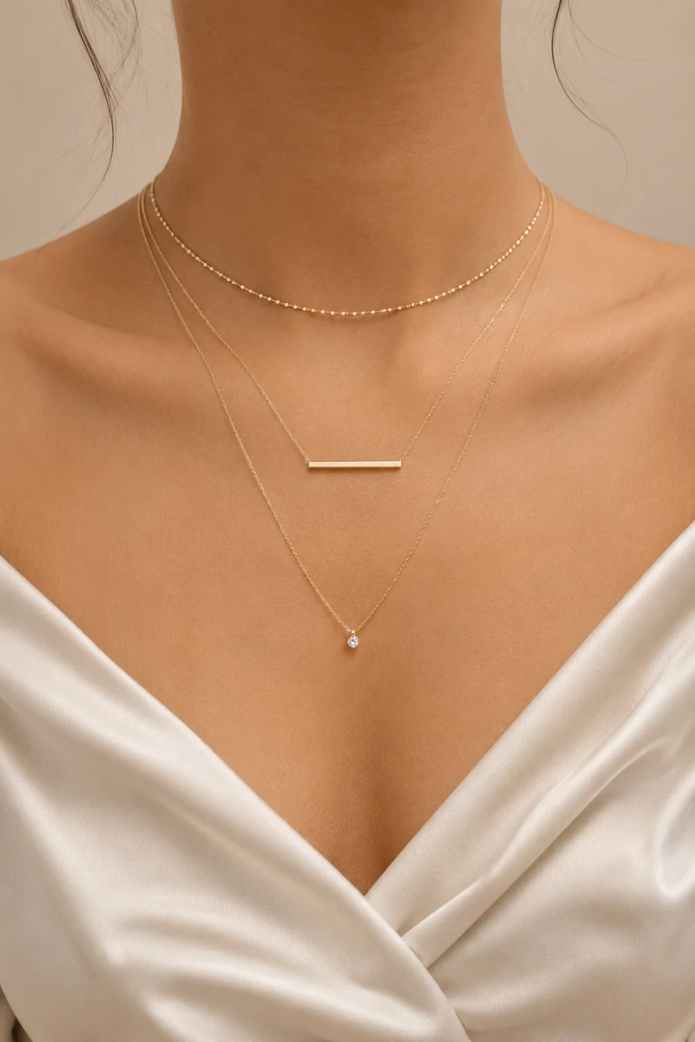 Woman wearing layered gold necklaces with a minimalist bar pendant and crystal charm styled with an elegant satin outfit.