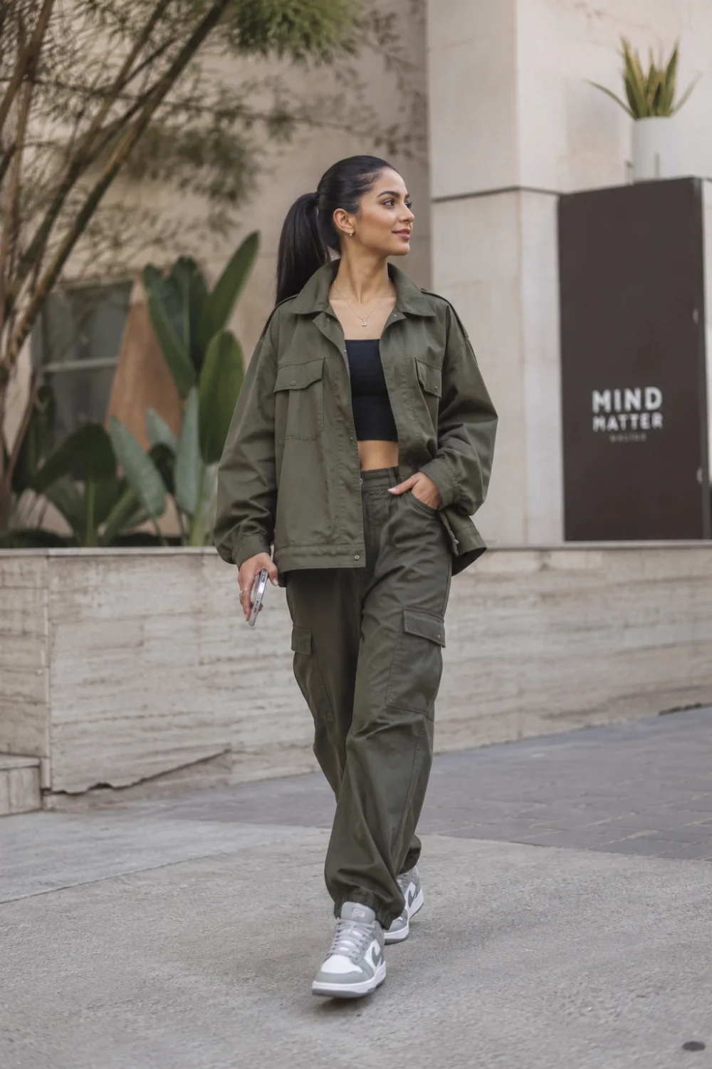 Modern woman wearing an oversized olive utility jacket with matching cargo pants and sneakers in an urban setting. Trendy oversized streetwear outfit featuring cargo fashion, relaxed silhouettes, and contemporary styling.
