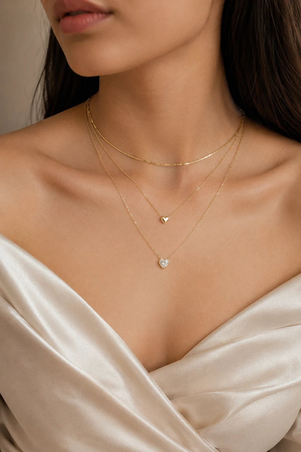 Woman wearing heart charm layered necklaces with delicate gold chains and sparkling heart pendants styled with a satin top.