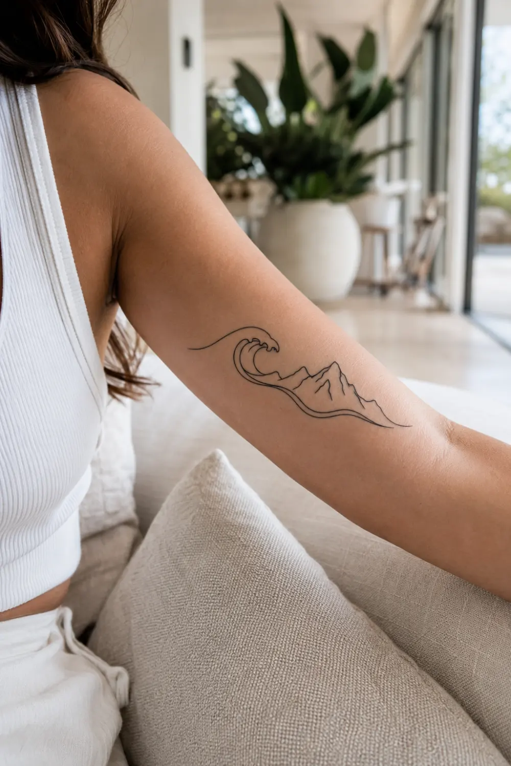 Mountain and wave tattoo on a woman's forearm featuring minimalist landscape line art, ocean and mountain tattoo design, fine line adventure tattoo, feminine body art inspiration, and elegant black ink artwork.