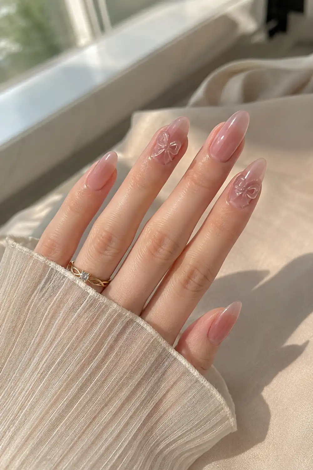 Pink jelly almond nails with 3D gel bow accents, glossy translucent finish, elegant almond shape, and feminine Korean-inspired nail art details.