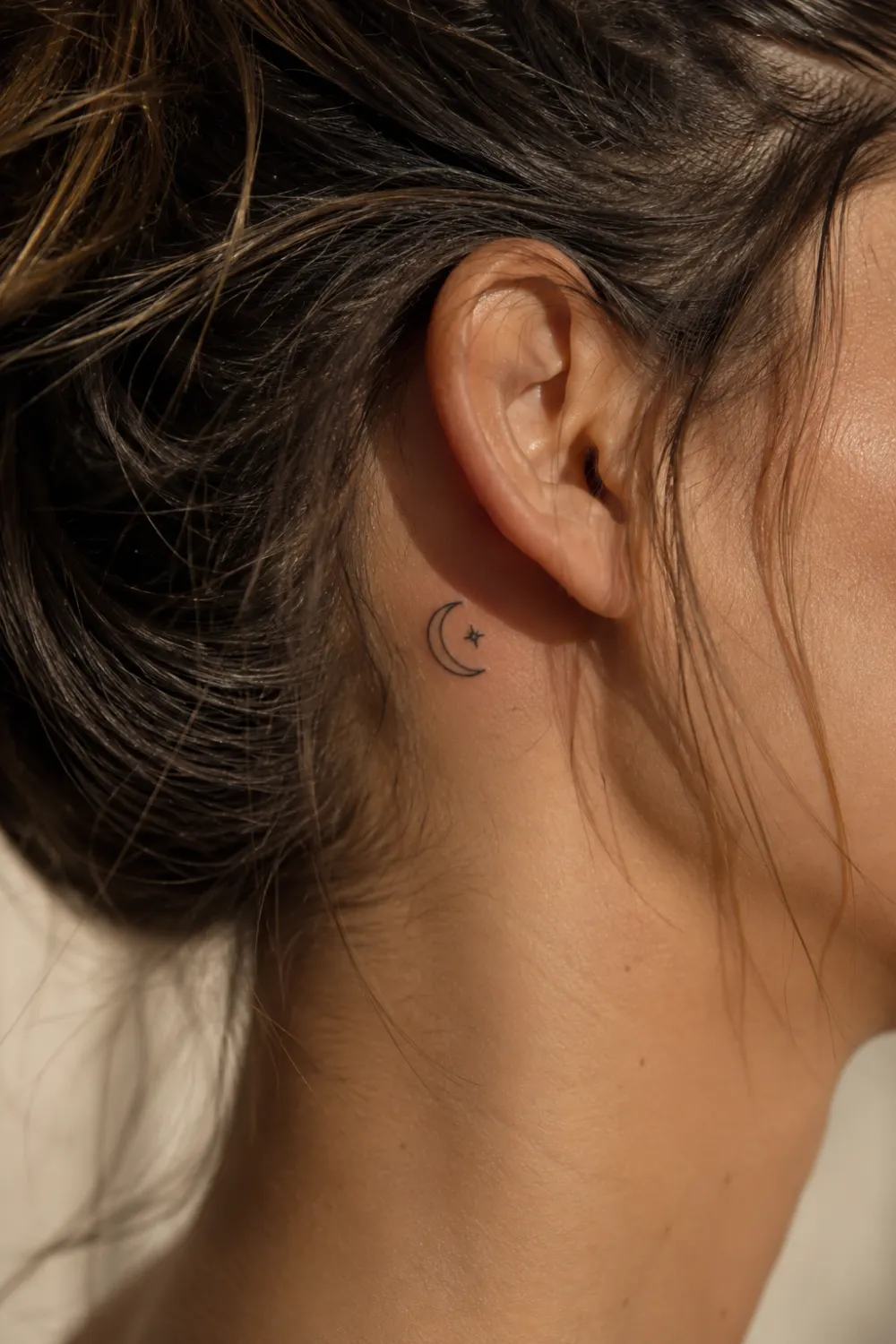 Minimalist moon and stars tattoo behind a woman's ear featuring delicate fine line celestial artwork, tiny crescent moon tattoo, feminine tattoo design, elegant black ink details, and subtle aesthetic body art inspiration.