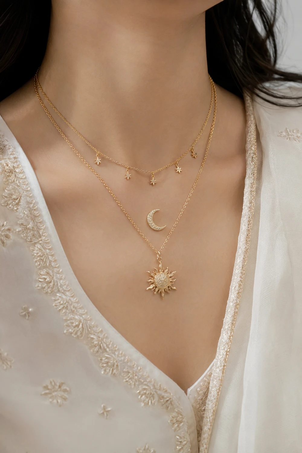 Woman wearing celestial layered necklaces with moon, star, and sun pendants paired with a cream embroidered outfit for a trendy jewelry style.