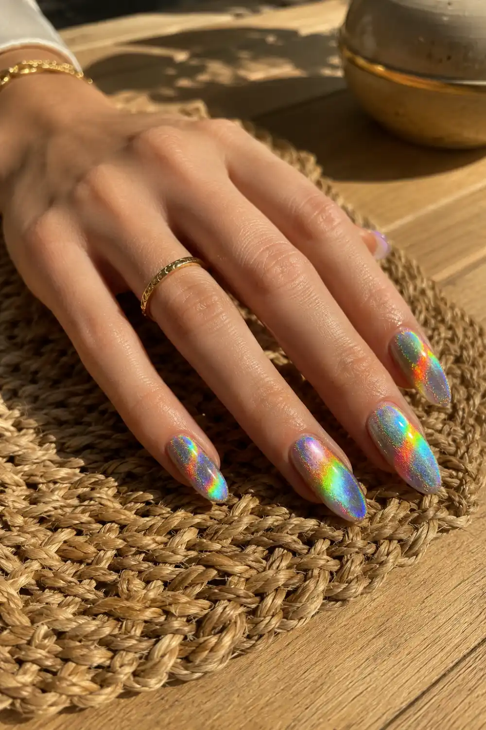 Rainbow chrome cat eye nails with holographic reflections and colorful shimmer on almond-shaped nails, displayed on a feminine hand resting on a woven rug in bright natural light.