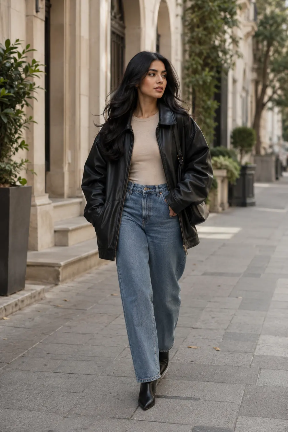 Stylish woman wearing an oversized black leather jacket with straight leg jeans and black ankle boots while walking through a luxury city street. Modern oversized leather jacket outfit featuring edgy fashion, classic denim styling, and trendy streetwear inspiration.